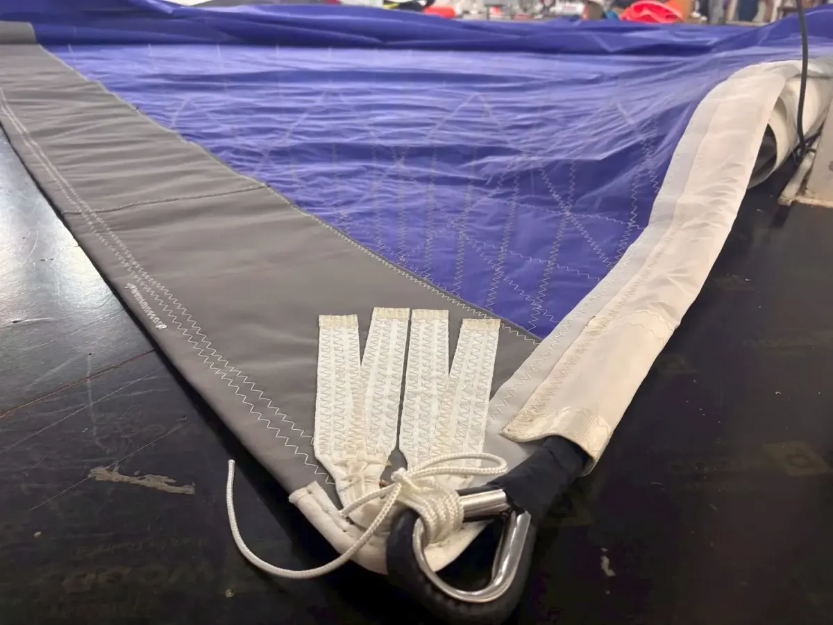 Tack of a blue code zero with webbing straps into a stainless shackle and the anti torsion luff running away