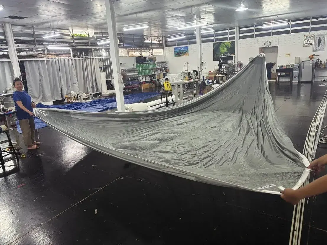 Sailmakers holding a silver asymmetric spinnaker open across the loft floor with sewing stations behind