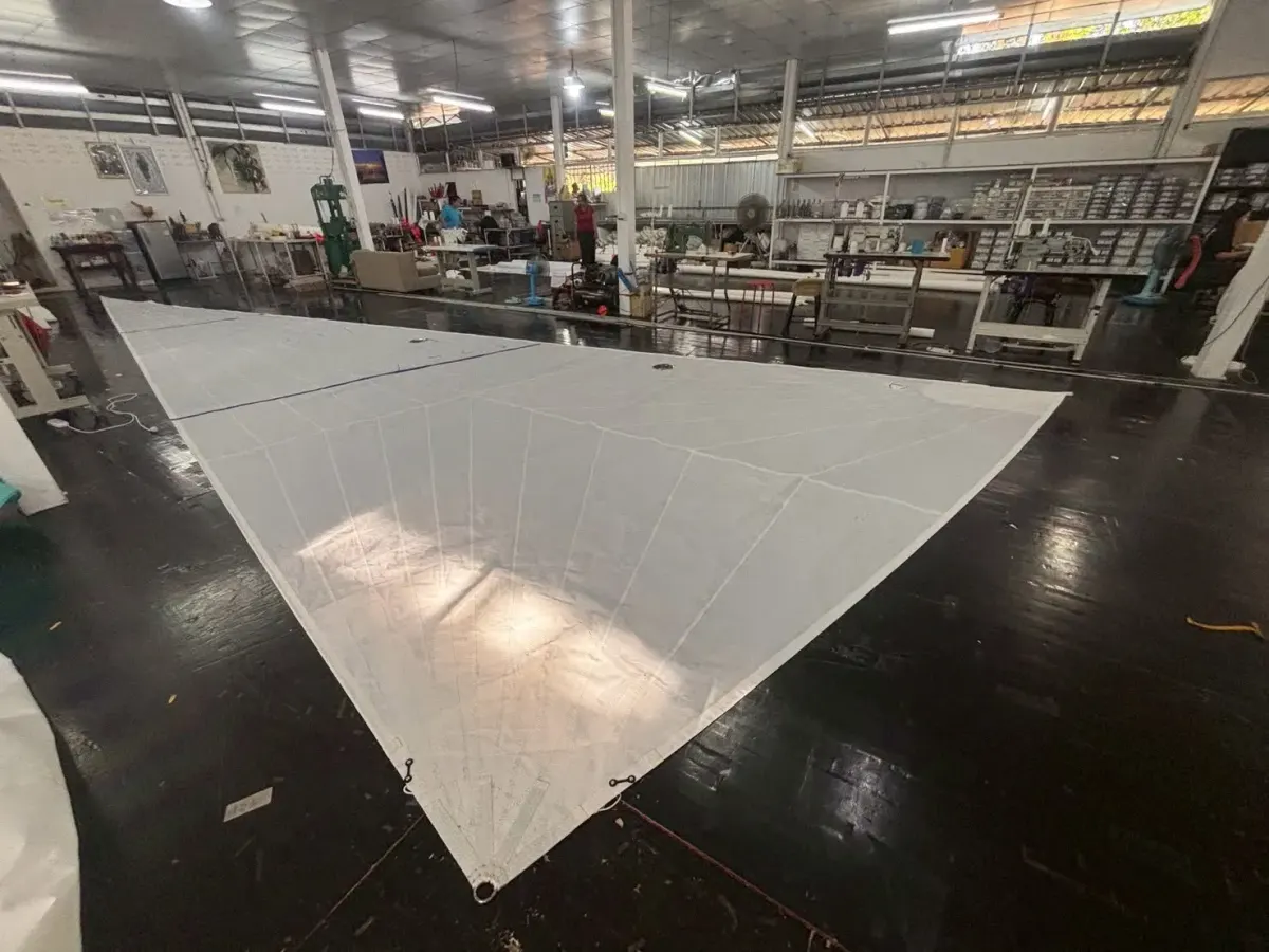 Complete white jib laid out on a black loft floor with workbenches and cloth racks behind