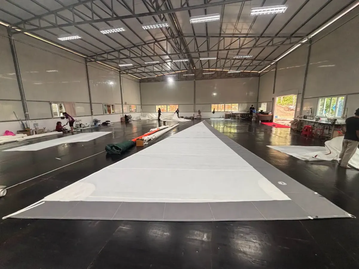 Very large genoa laid out down the length of a bright loft hall with sailmakers working on other sails