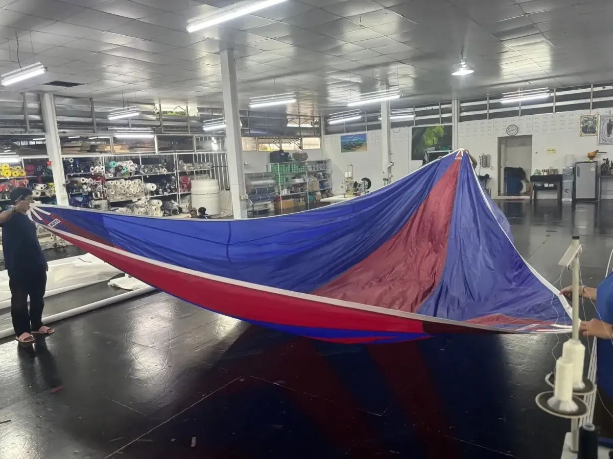 Two sailmakers holding a red and blue symmetrical spinnaker open across the loft floor