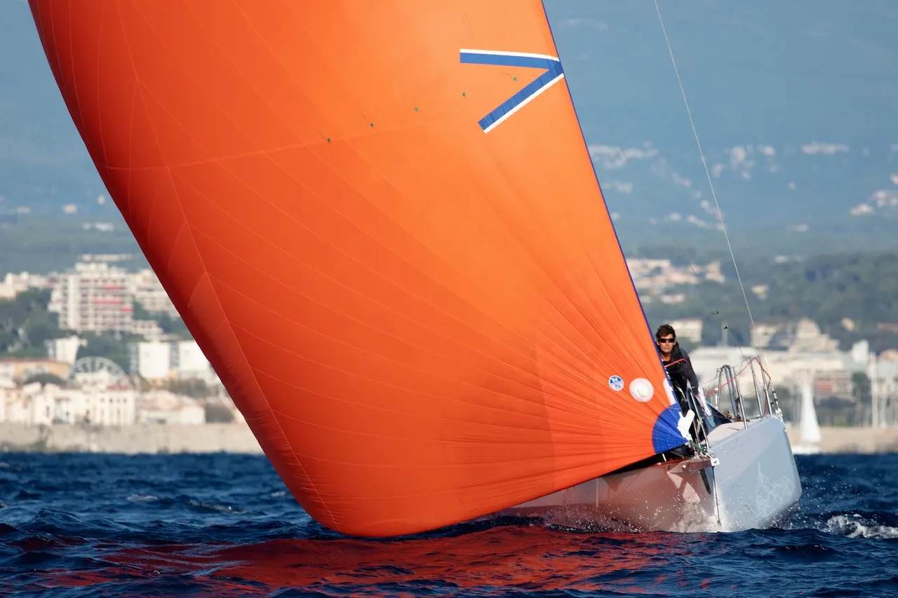 A vibrant, fully deployed spinnaker sail is billowing on a sailboat as it sails downwind over clear blue water