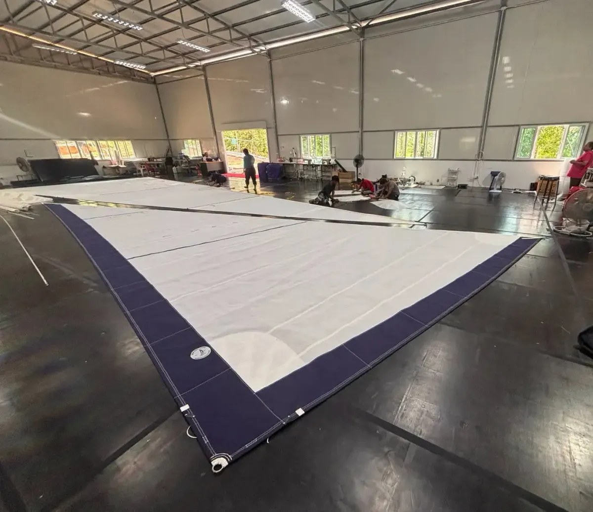 Complete headsail with a navy UV cover laid out across a bright loft floor with sailmakers working behind