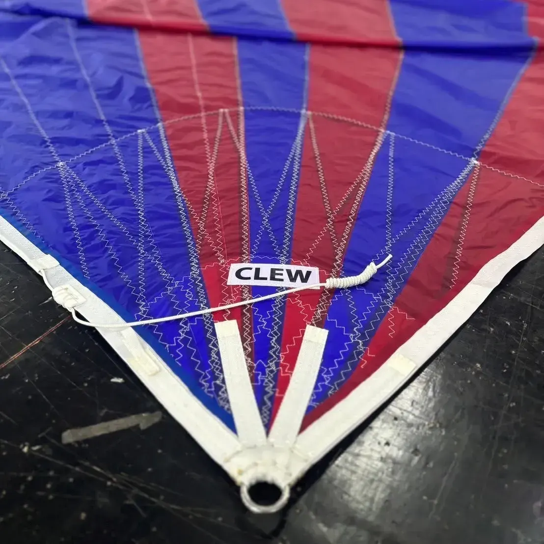 Clew of a red and blue striped spinnaker showing radial fan stitching, webbing straps and a sewn ring