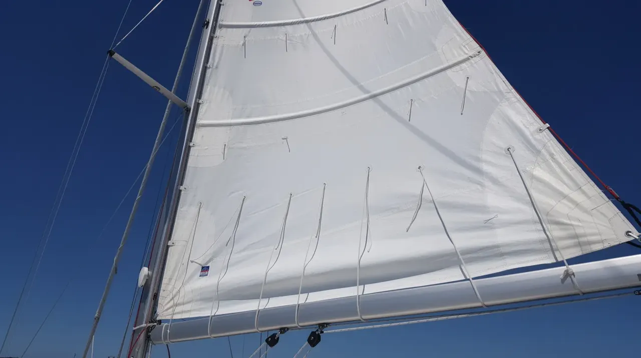 A close-up view of a mainsail on a sailboat showcases its intricate sail cloth, featuring visible battens and reef lines