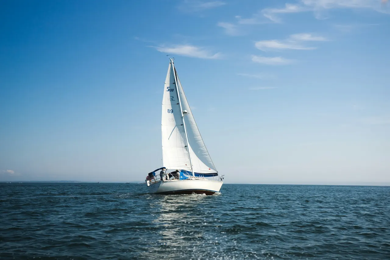 A sailing yacht is heeling dramatically under full sails, gliding through the open ocean with a clear blue sky above