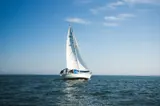 A sailing yacht is heeling dramatically under full sails, gliding through the open ocean with a clear blue sky above
