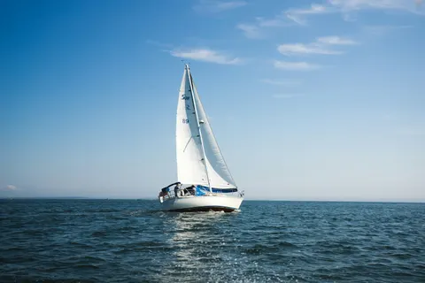 A sailing yacht is heeling dramatically under full sails, gliding through the open ocean with a clear blue sky above